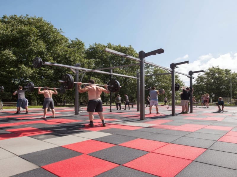 Eine kniende Person verlegt Gummifliesen für den Außenbereich auf einem vorbereiteten Schotteruntergrund.